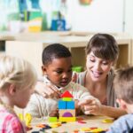 Teacher helping children play with building blocks in a bright daycare setting