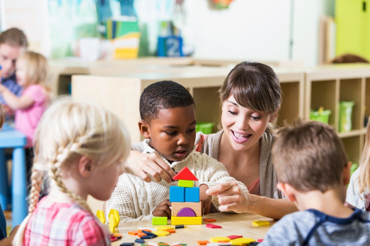 Teacher helping children play with building blocks in a bright daycare setting