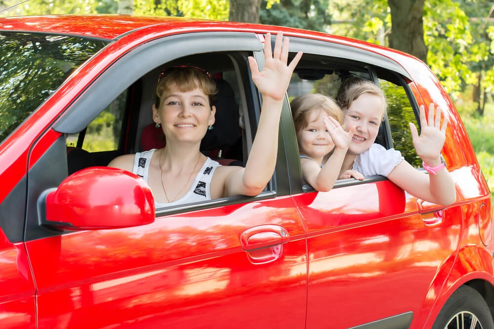 Single mom smiles with her children next to their donated car.