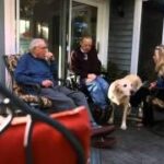 Three people sitting on a porch with a dog, representing the community aspect of Veterans Foster Care