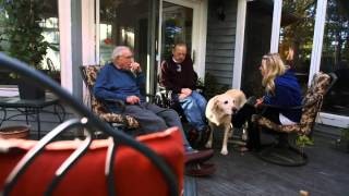 Three people, including a veteran and caregiver, sitting on a porch with a dog, symbolizing the comforting home environment of the VA foster care program.