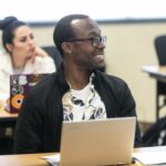 Smiling male student with laptop in classroom.